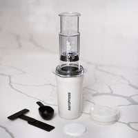 Aeropress coffee maker with components on a marble surface