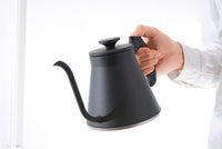 Person holding a black kettle against a white background